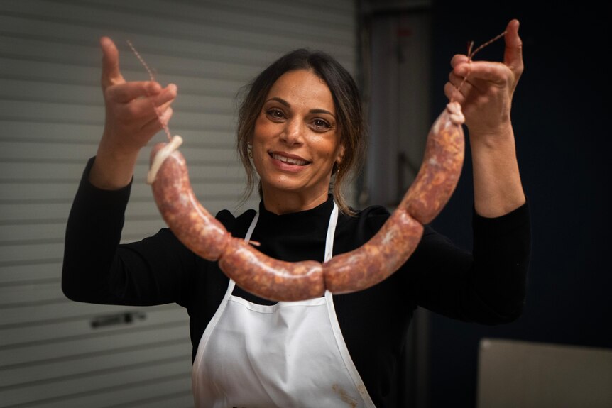 A woman smiles holding up sausages