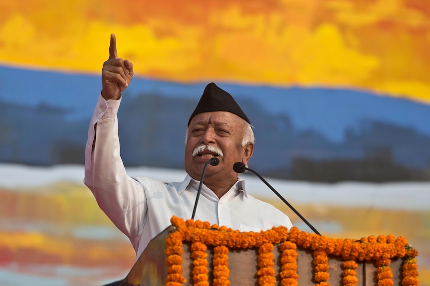 An Indian man speaks at a podium with his finger pointing into the air. 