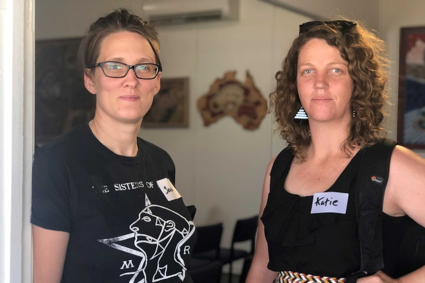 Two fair-skinned young women wear black clothing and look plainly at the camera