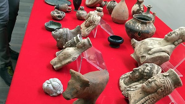 A table covered with a red tablecloth has dozens of historic artefacts placed on it