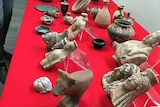 A table covered with a red tablecloth has dozens of historic artefacts placed on it