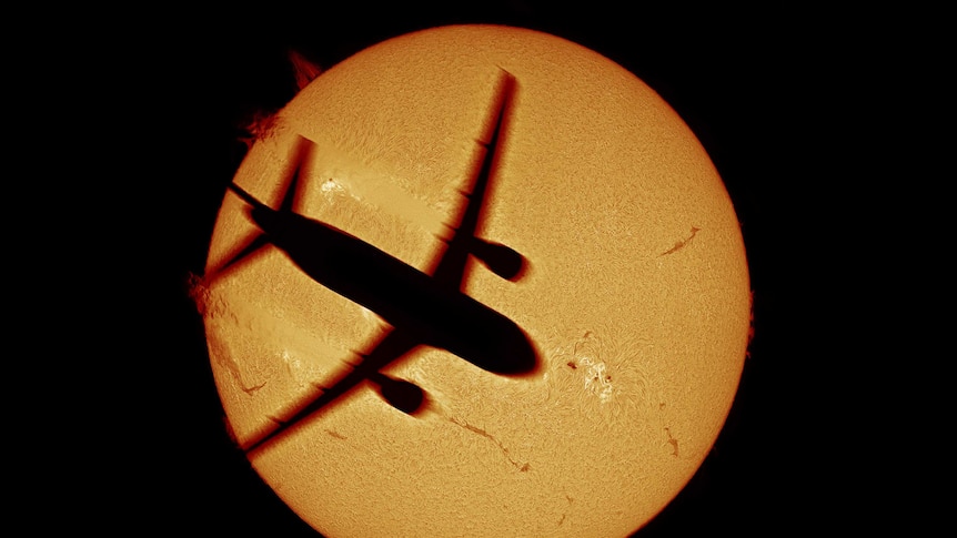 Black outline of an aeroplane flying across the outline of the sun or a planet