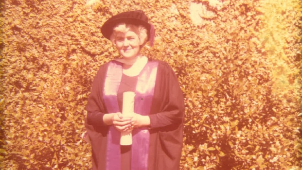Ann Shorten wears academic robes and a hat as she stands with her law degree