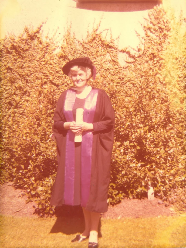 Ann Shorten wears academic robes and a hat as she stands with her law degree