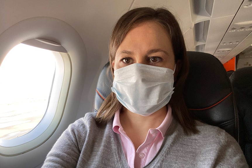 Photo of reporter Rachel Pupazzoni on a plane wearing a protective mask.