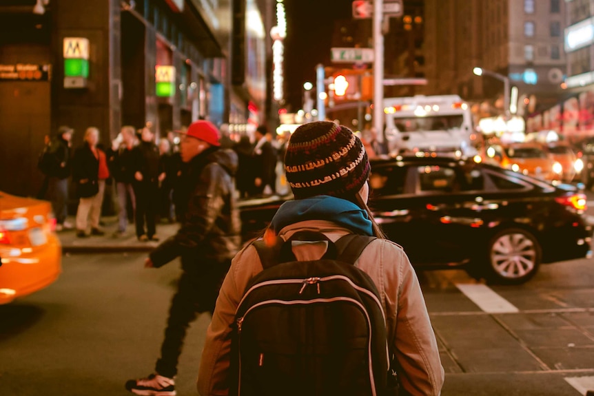 A woman wearing a beanie and a backpack walks on a busy street.