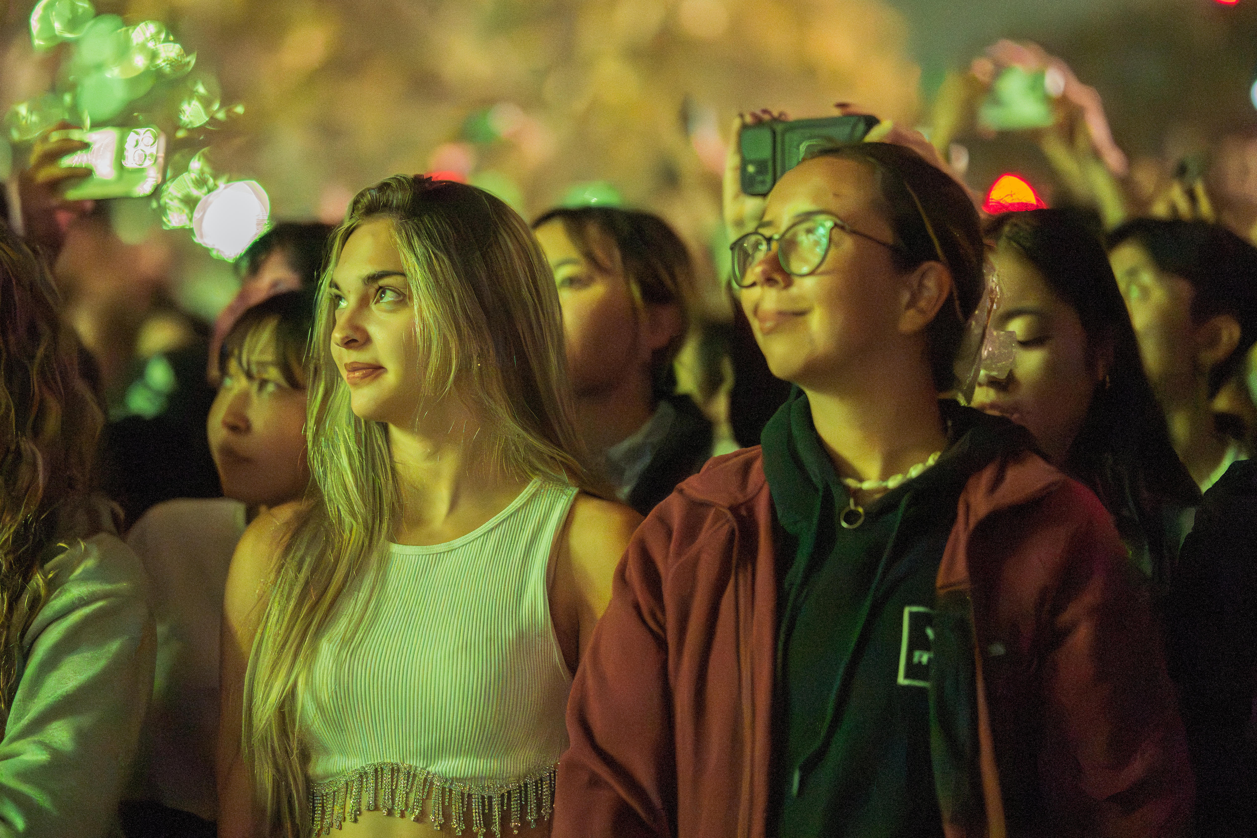 Dos mujeres entre la multitud sonríen mientras los fuegos artificiales las iluminan.