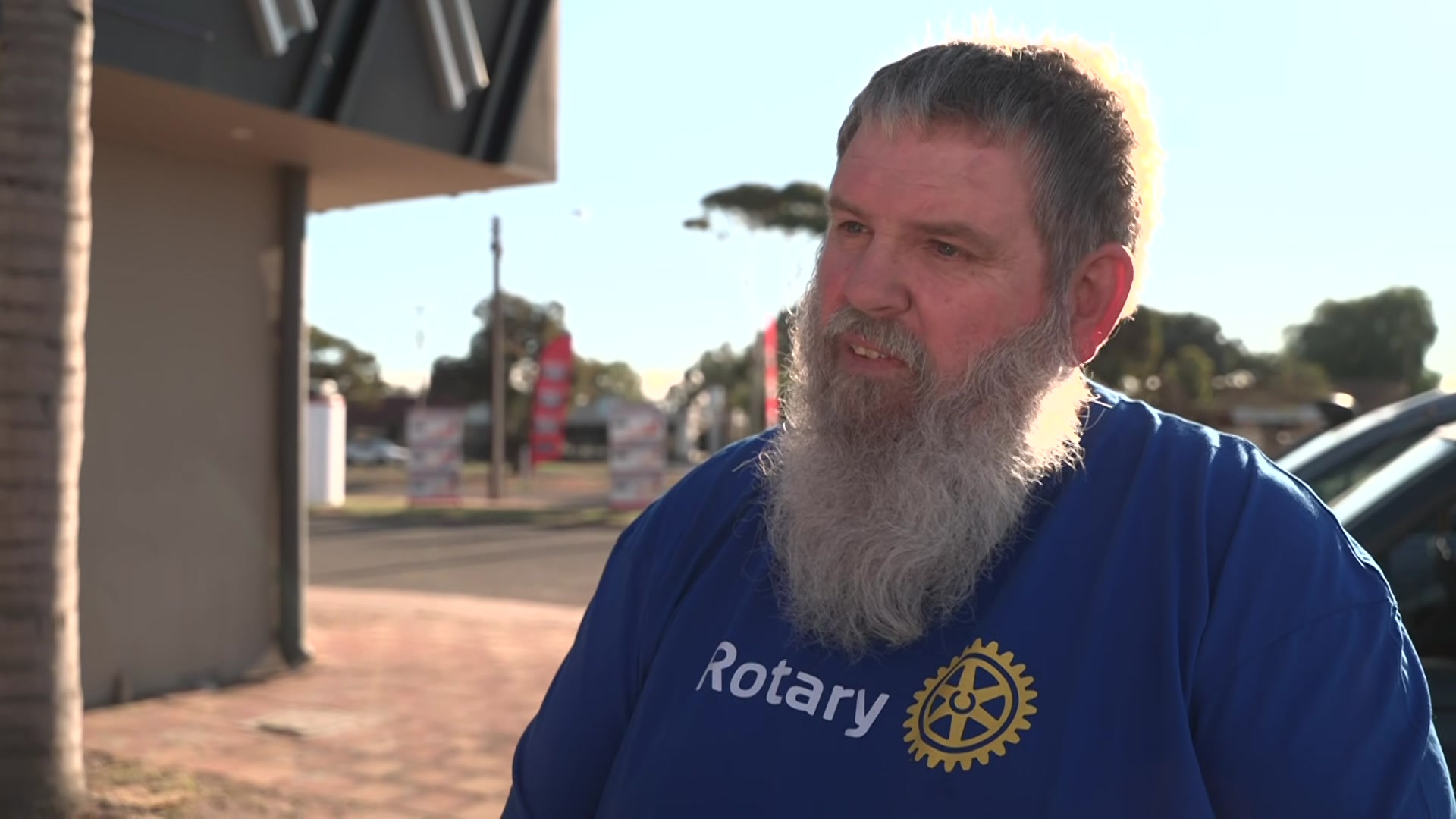 A man in a blue t-shirt and beard is standing on a footpath.
