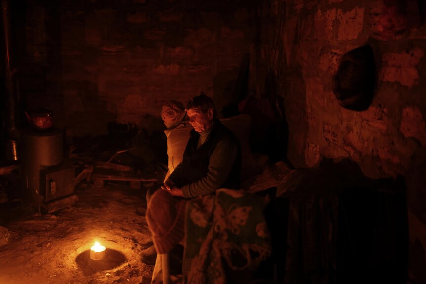 A person sits on the edge of a bed in front of a fire that is burning inside. 