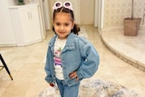 A young girl posing in a denim jacket and novelty sunglasses. 