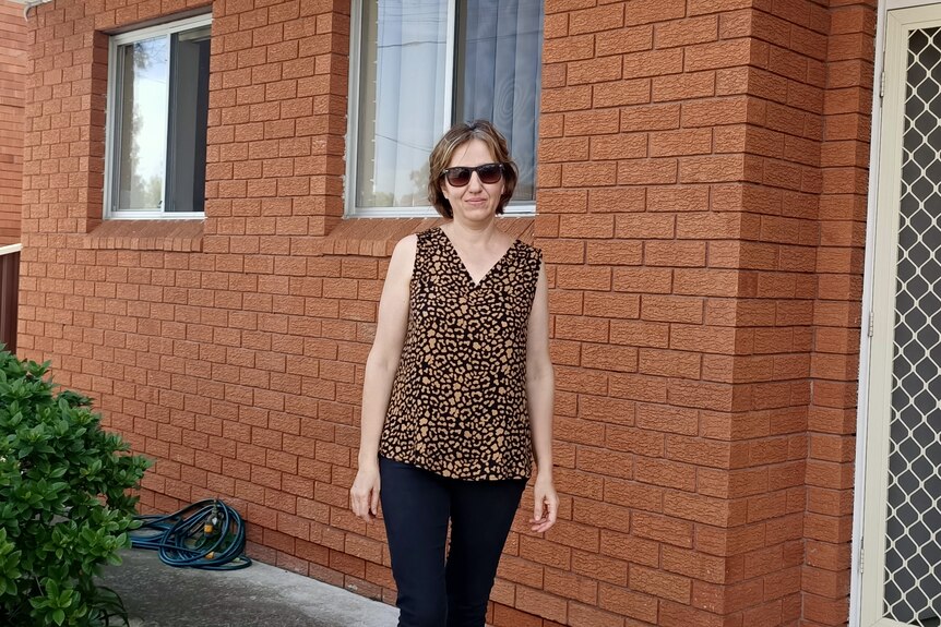 Olga Palanska wearing sunglasses and standing in front of a brick apartment building.