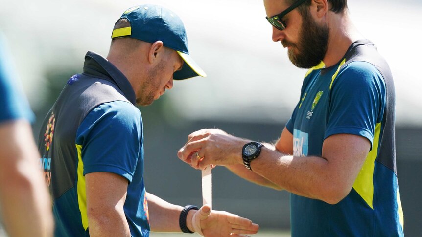 David Warner holds his hand out while a man unwinds some strapping tape.