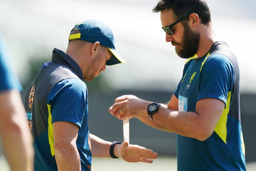 David Warner holds his hand out while a man unwinds some strapping tape.