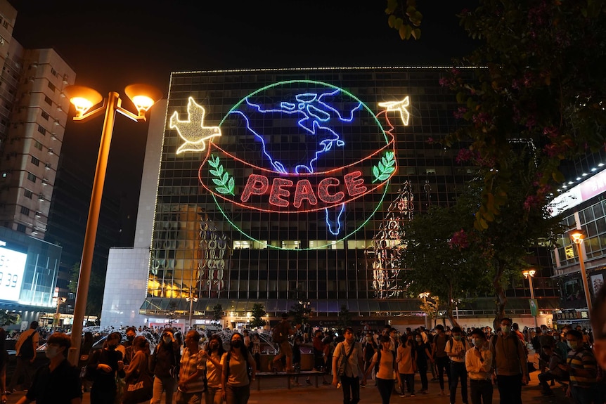 A high-rise building has a large neon sign showing the earth with peace written over it.