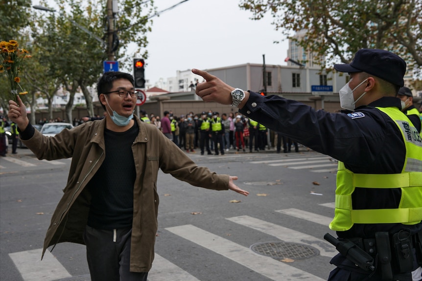 A protester holding flowers is confronted by a policeman during a protest on a street.