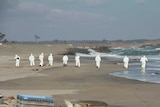 Police in white suits searching the beach