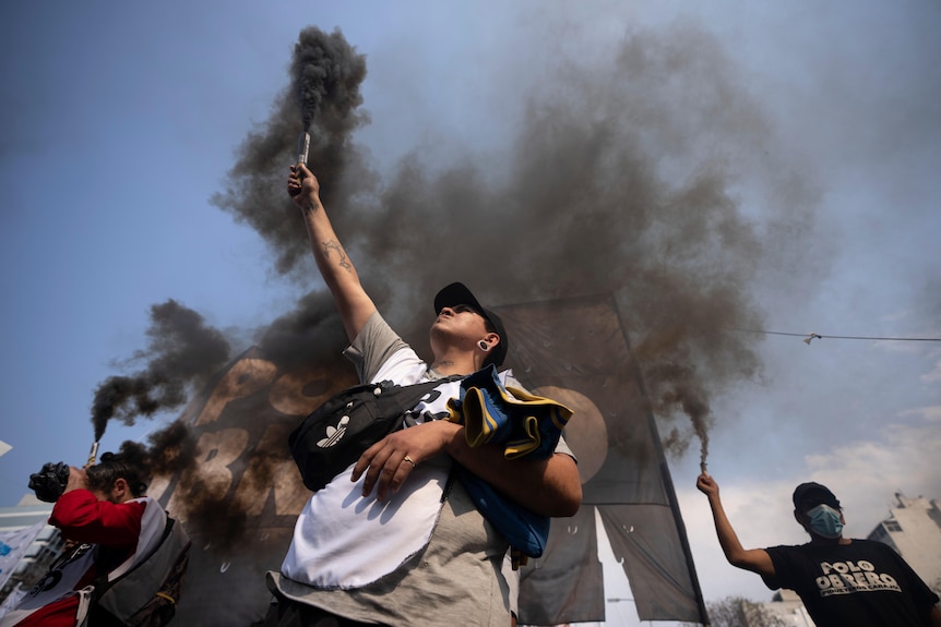 Demonstrators look to the clear sky as they light flares that release a thick dark grey smoke.