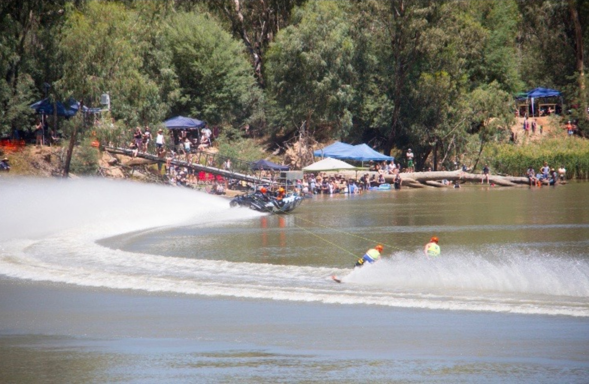 Un barco arrastra a dos esquiadores en un río frente a los espectadores en la orilla del río.