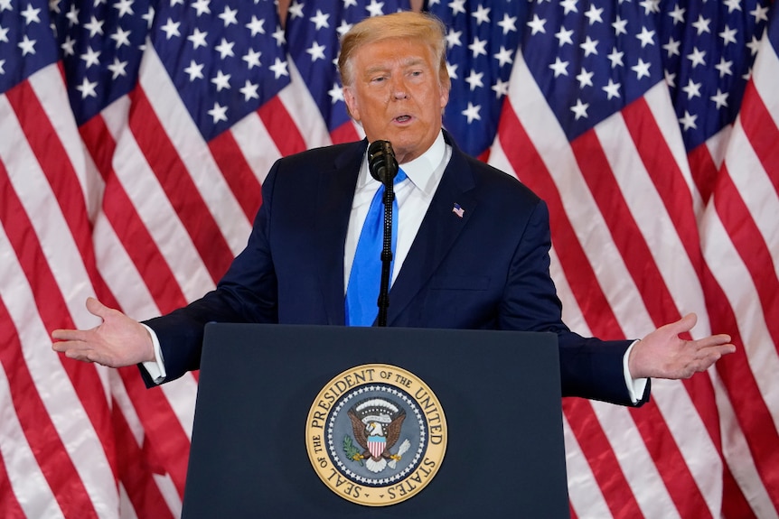 US President Donald Trump speaking at a lectern, wearing a suit