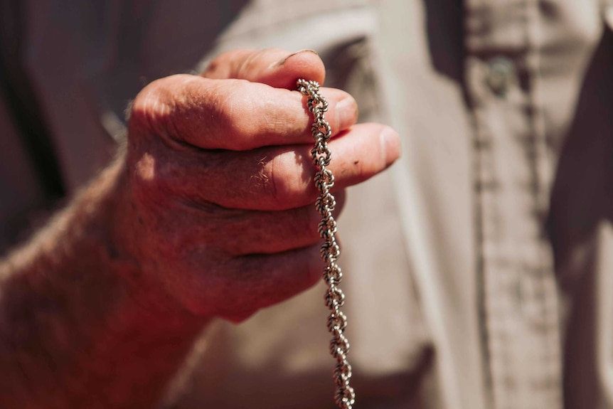 A close-up of an old man holding a gold necklace which he uses for gold divining.