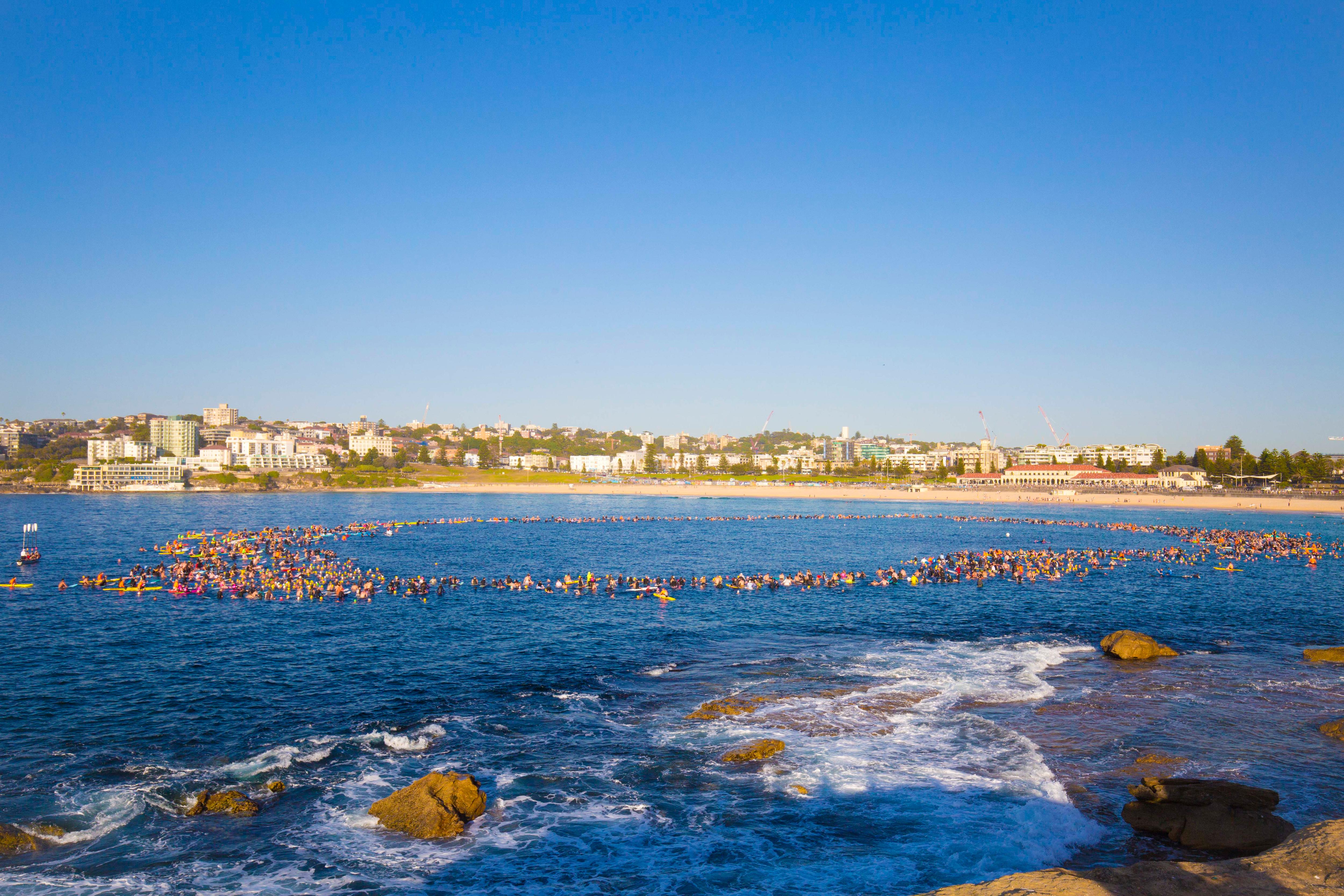 Un gran grupo de nadadores y practicantes de remo forman un círculo en el agua en North Bondi.