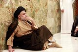 Mr al-Sadr sits on the floor, his hand resting at his mouth