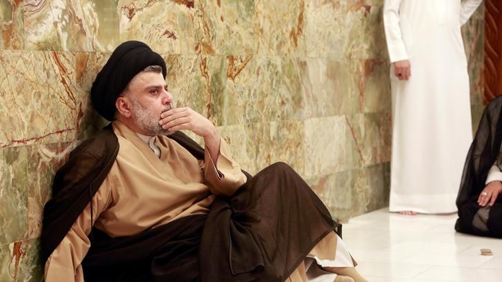 Mr al-Sadr sits on the floor, his hand resting at his mouth