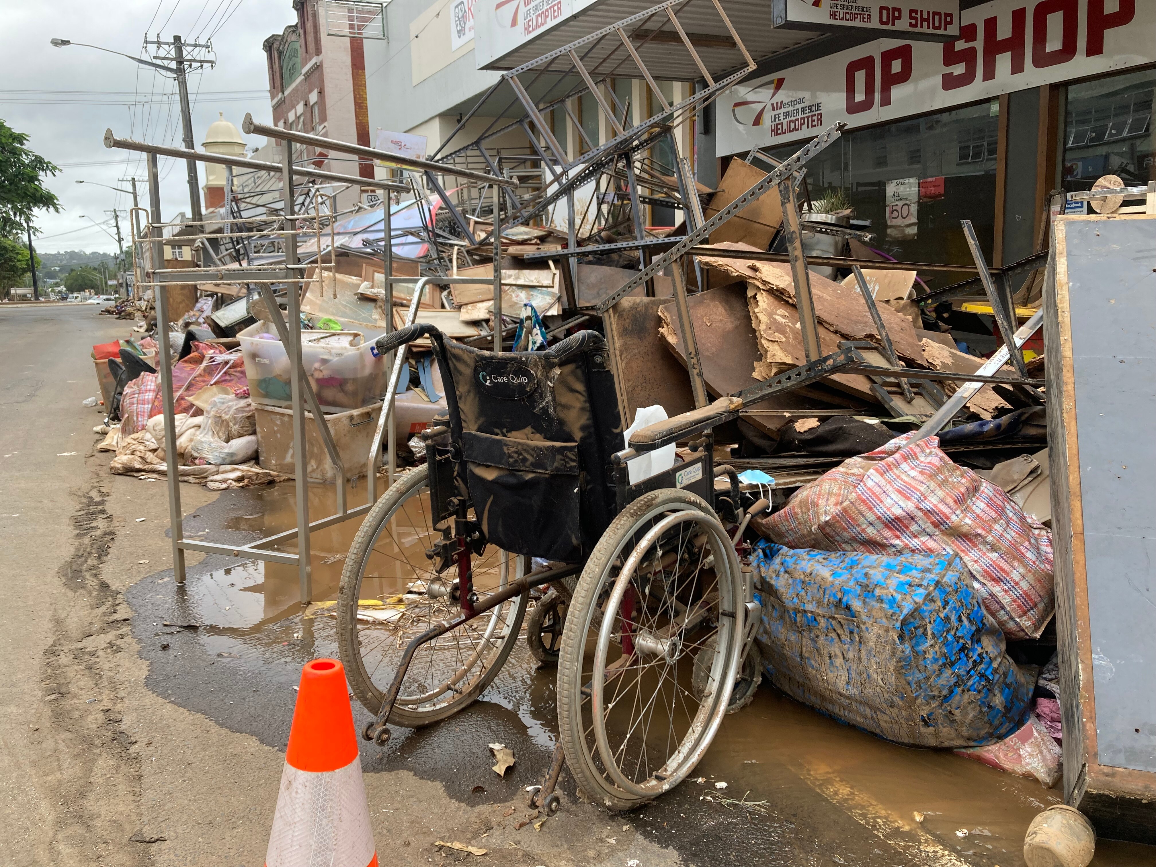 A wheelchair among debris and rubbish covered in mud.