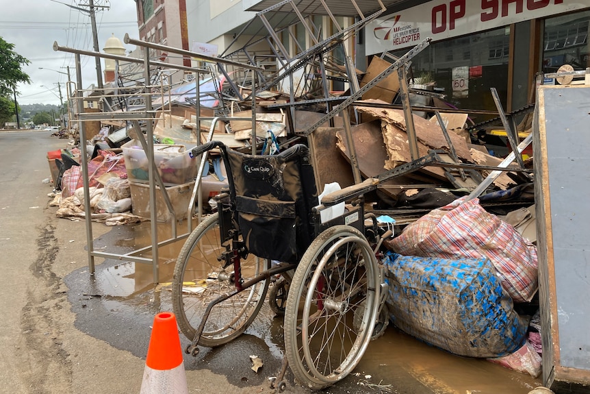 A wheelchair among debris and rubbish covered in mud.