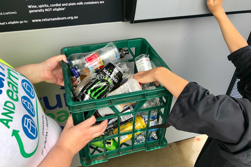 Recycling officer and child holding a carton of containers to deposit into a reverse vending machine