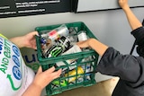 Recycling officer and child holding a carton of containers to deposit into a reverse vending machine