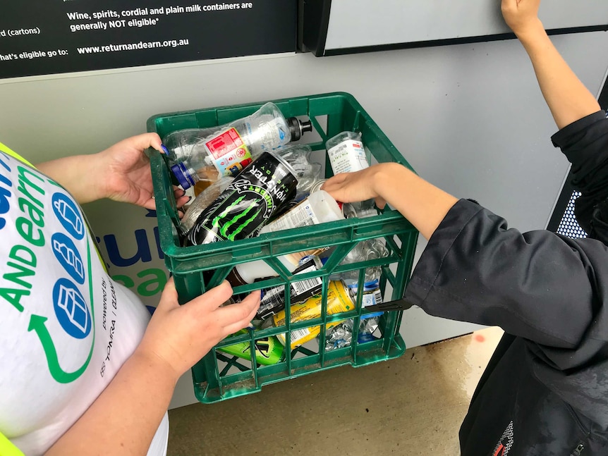 Recycling officer and child holding a carton of containers to deposit into a reverse vending machine