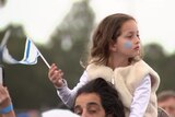 Girl with Star of David painted on her cheek sits on a man's shoulders waving Israeli flag