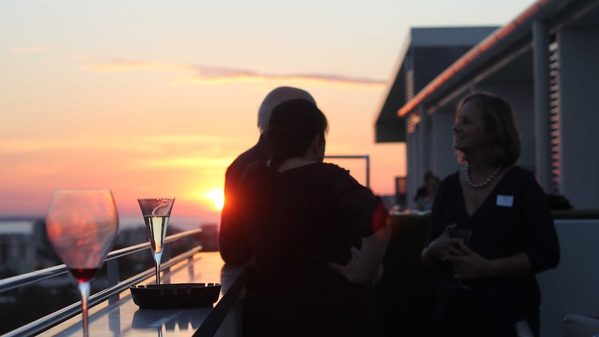 People at a sunset cocktail party take photos of each other.