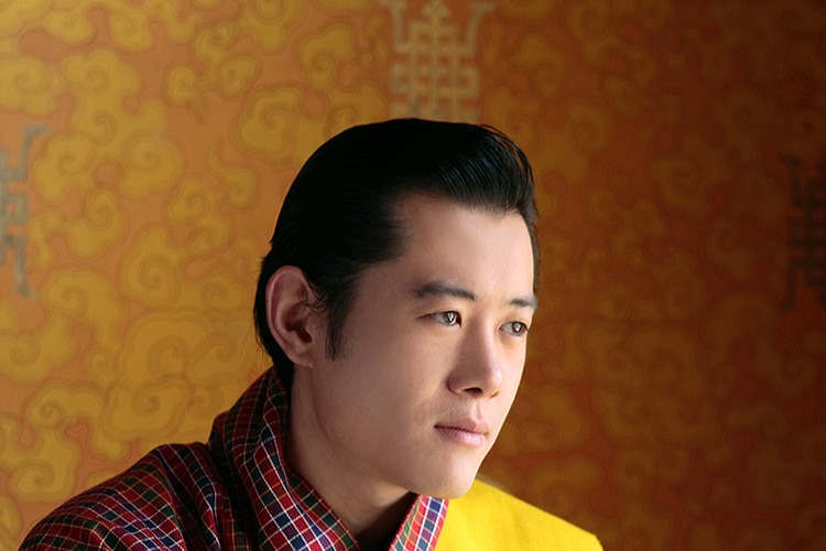 King Jigme Khesar Namgyel Wangchuck wearing a traditional Bhutanese robe with a bright yellow sash.