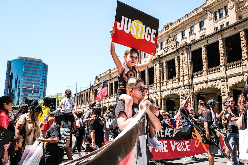 A child sat on a woman's shoulders holding a sign