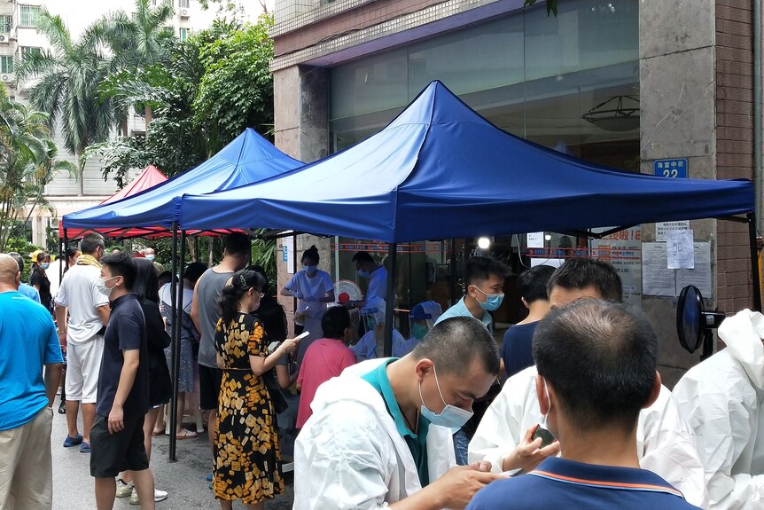 Residents of Guangzhou, many wearing face masks, queue outside to be swabbed for a COVID test.