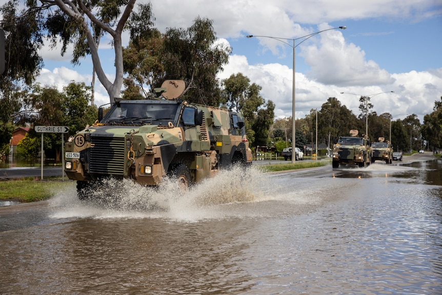 A military vehicle drives through flood waters on a highway