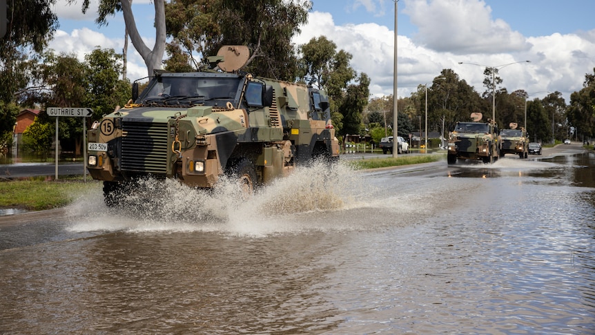 A military vehicle drives through flood waters on a highway