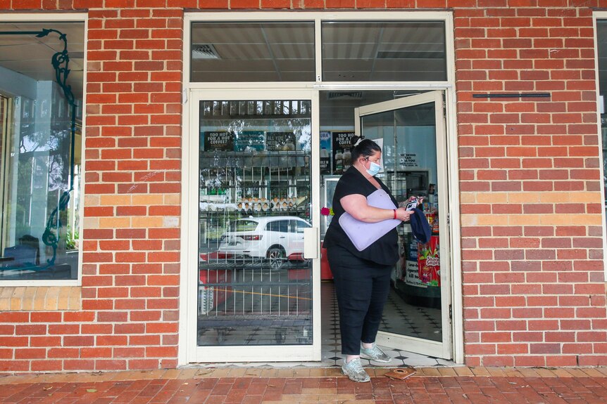 A woman closes a shop door. The facade is brick with no signage