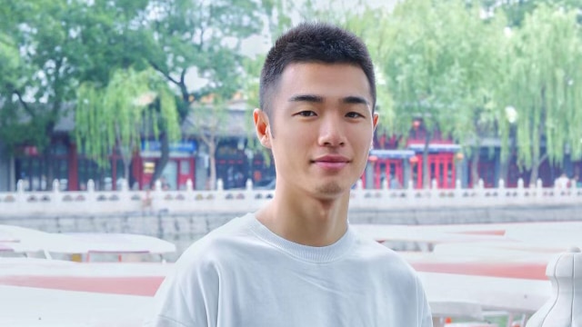 Chinese international student Zhang Yiming stands outside posing for a photo. 