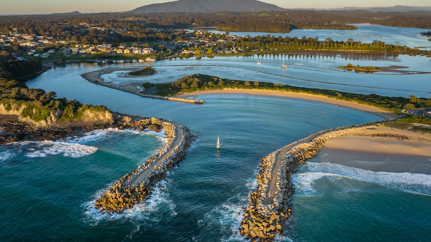 A drone image shows the bar crossing with a small boat heading through it, and a mountainous vista in the background.