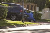 A forensic officer takes a photo of the back of a car in front of a house where a man was fatally shot.