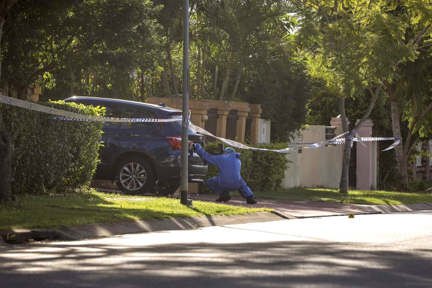 A forensic officer takes a photo of the back of a car in front of a house where a man was fatally shot.