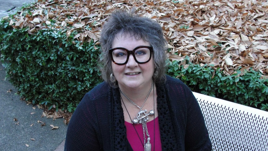 A lady with thick-rimmed glasses and grey hair smiling at the camera