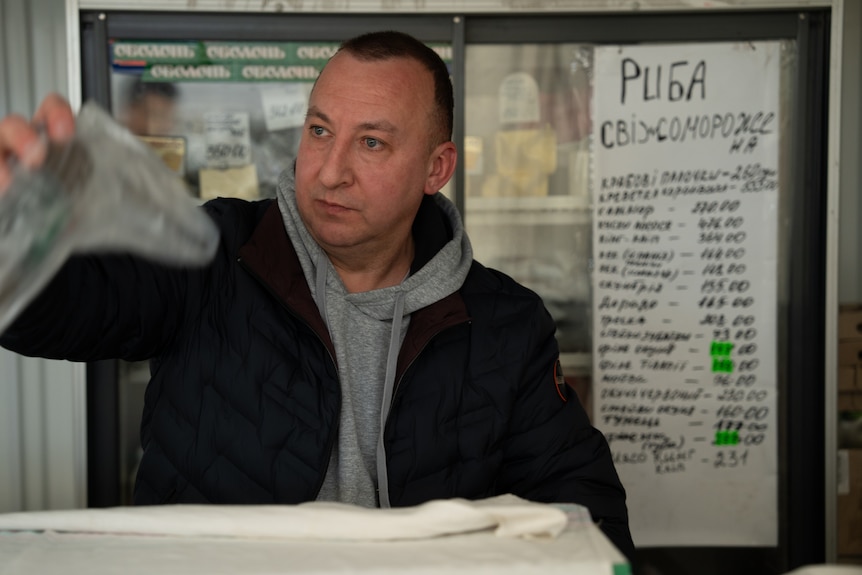 Man in grey hoodie and black jacket working at a shop.
