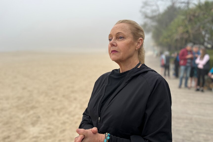 A woman stands on a beach looking soulfully