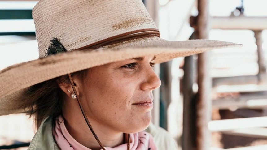A young woman wearing a straw hat looking out across the stockyards