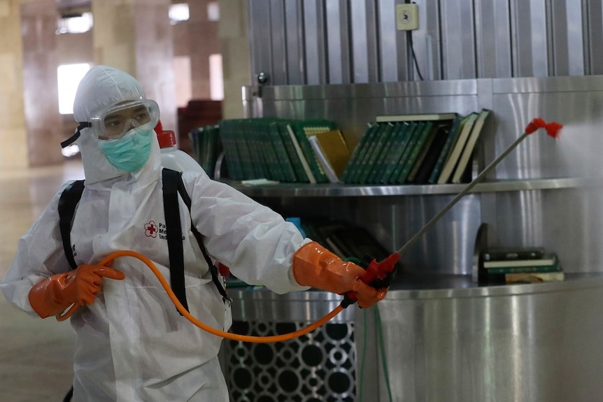 An official in protective gear disinfects a  mosque.