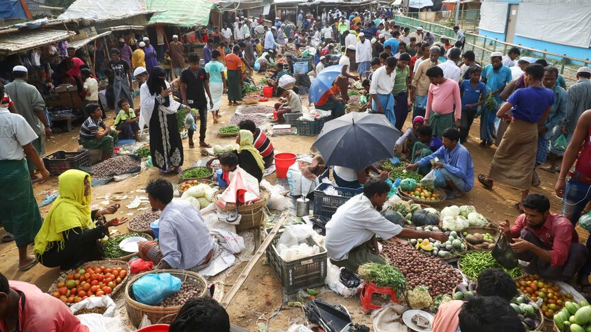 A busy market with umbrellas and fruit laid out on the ground as people mill around at Cox's Bazar refugee camp.